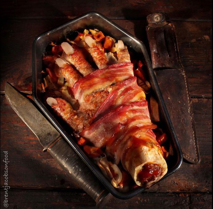 Creative Halloween meatloaf shaped like a human hand with bacon wrap, presented in a baking dish.