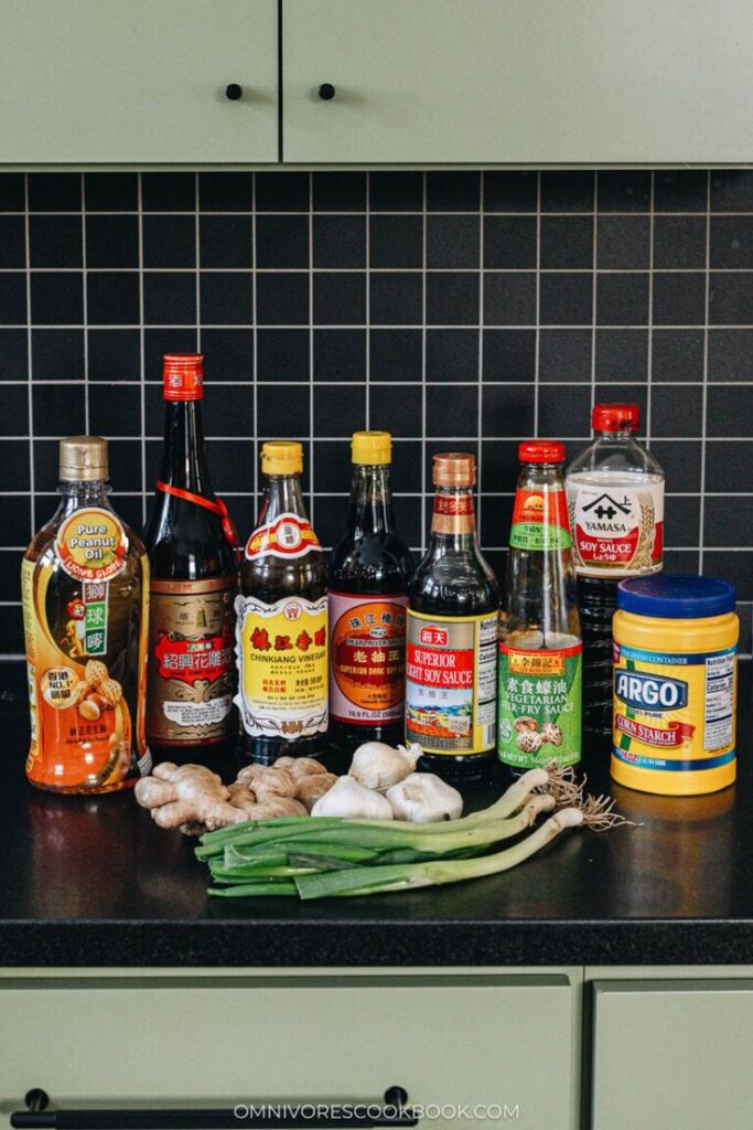 Assorted Asian cooking ingredients, including sauces, garlic, ginger, and green onions on a kitchen counter.