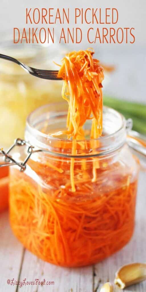 Korean pickled daikon and carrots in a jar, with a fork lifting strands, on a rustic wooden table.