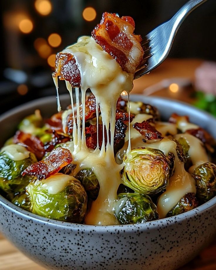 Cheesy Brussels sprouts with crispy bacon in a bowl, lifted by a fork, perfect for a delicious side dish.