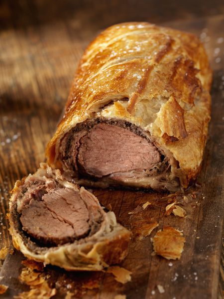 Beef Wellington with a golden crust on a wooden board, sliced to reveal tender beef inside flaky pastry.