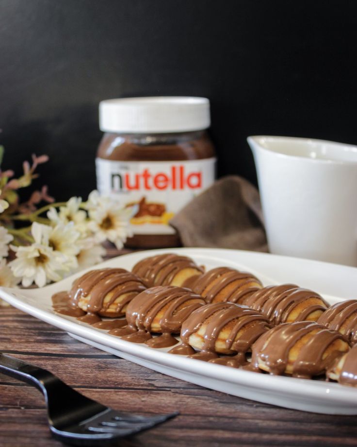 Plate of pastries drizzled with chocolate with a jar of Nutella in the background on a wooden table.
