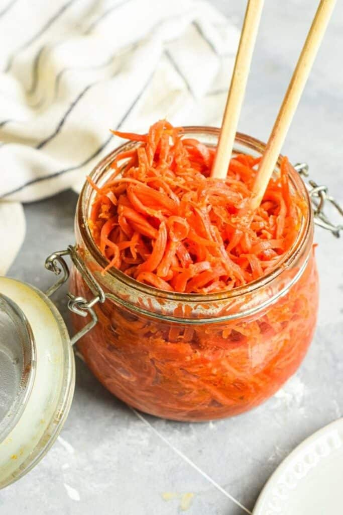 Glass jar filled with spicy pickled carrots and chopsticks on a kitchen counter.