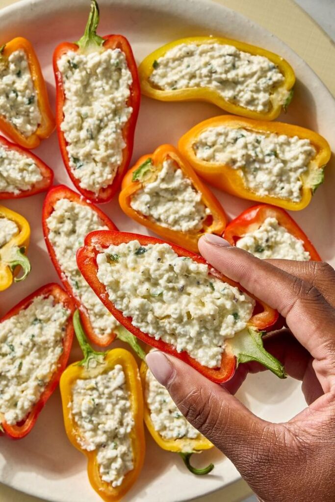 Need a Quick Snack_ Try These Mini Bell Peppers with Cottage Cheese - 10 Crowd-Pleasing Appetizers That Will Wow Your Party | Stuffed mini peppers with creamy filling on a plate, hand holding one. Perfect appetizer or snack idea.