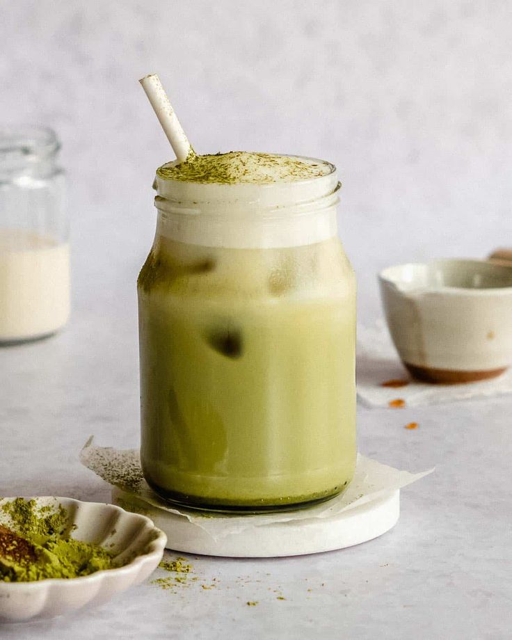 Iced matcha latte in a jar with a straw, topped with foam and matcha powder, on a white background.
