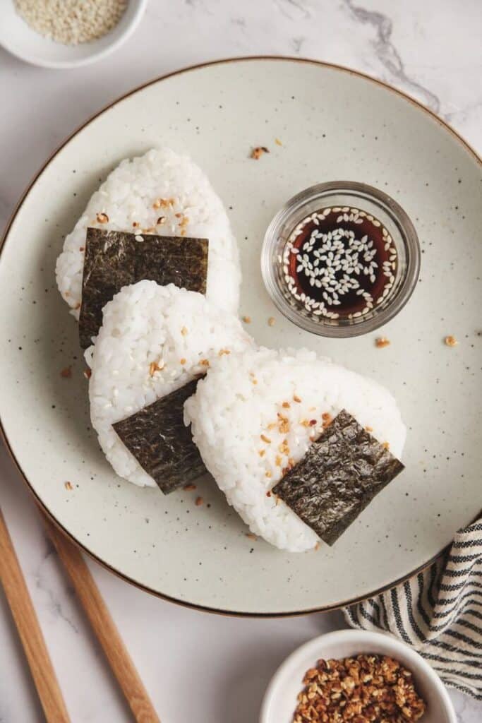 Japanese onigiri rice balls with nori, served with soy sauce and sesame seeds on a plate. Asian cuisine.