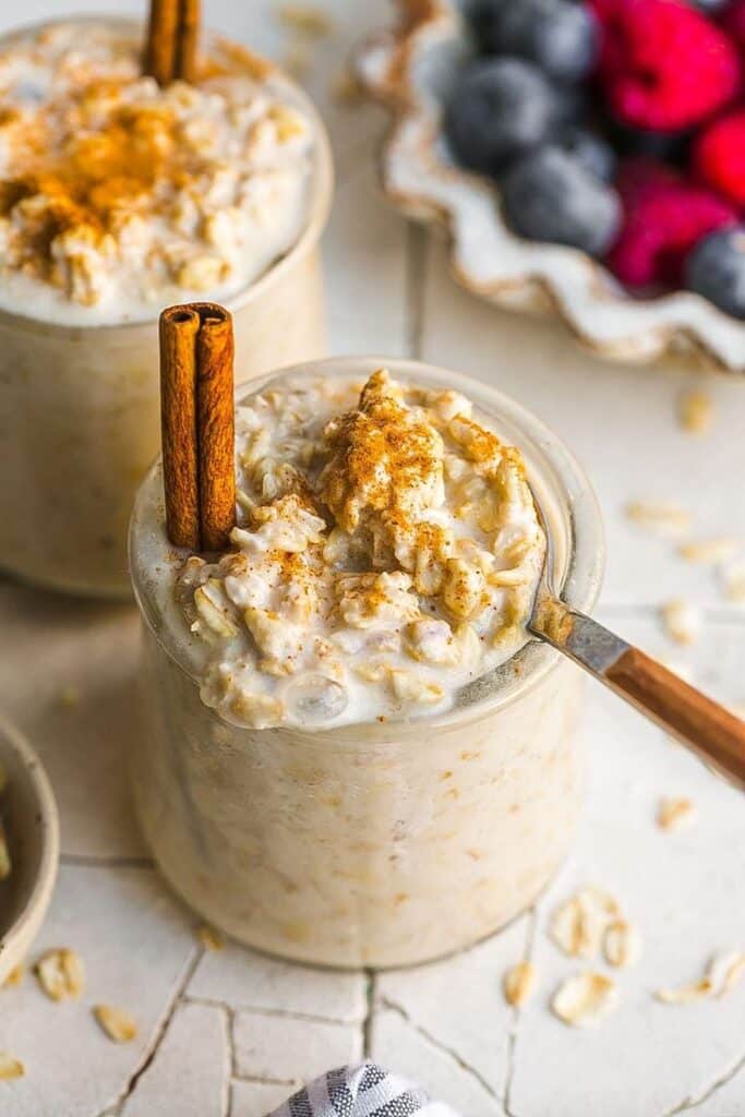 Creamy overnight oats topped with cinnamon and honey in a jar, with fresh berries on the side. Perfect breakfast idea.