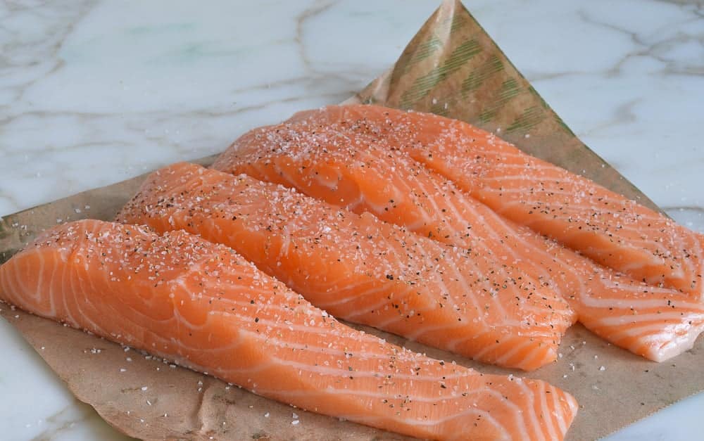 Fresh salmon fillets seasoned with salt and pepper on brown paper, ready for cooking on a marble surface.