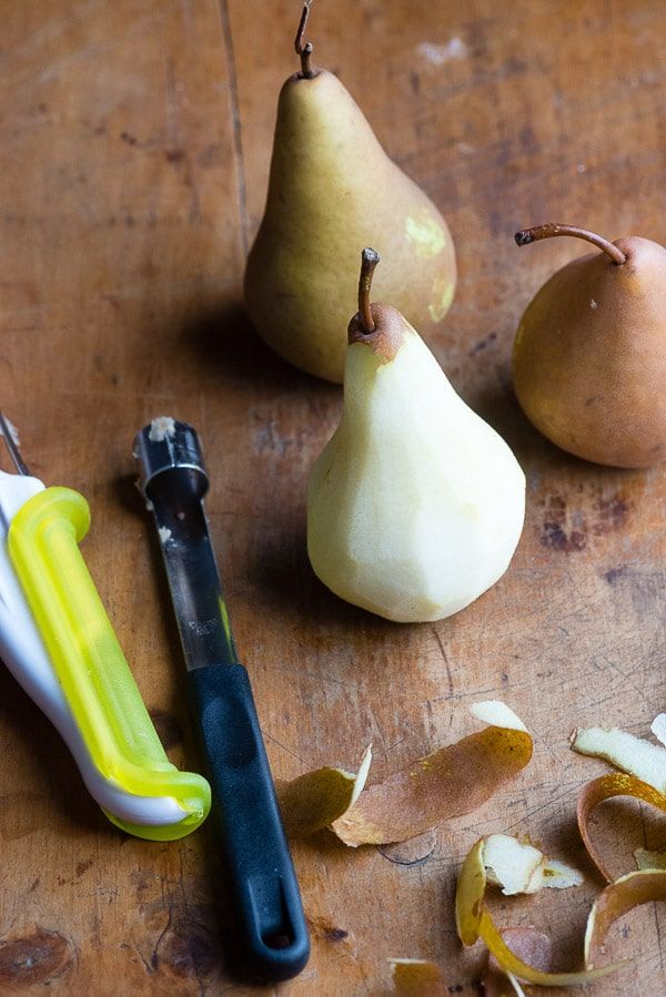 Whole and peeled pears with a peeler on a wooden surface.