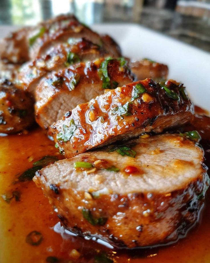Sliced grilled pork tenderloin with a savory herb glaze, served on a white plate.