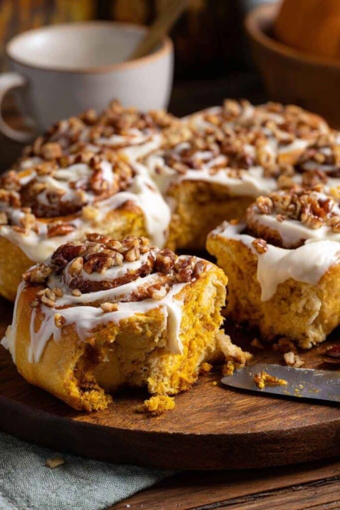Freshly baked cinnamon rolls topped with icing and pecans on a wooden serving board.