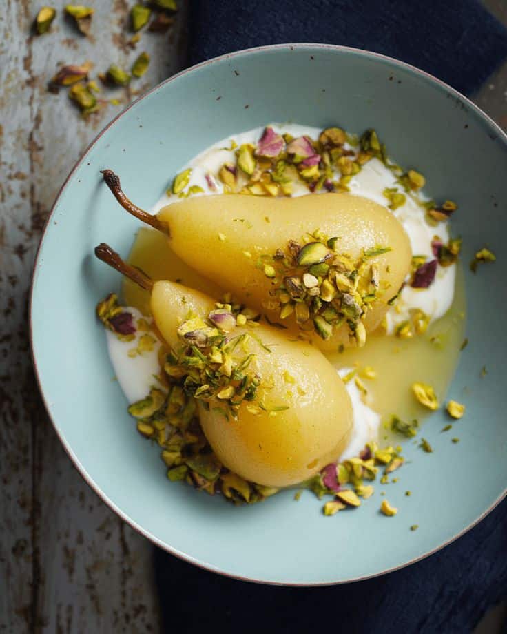 Poached pears with pistachios on a blue plate, served with creamy yogurt. Perfect for a healthy and elegant dessert.