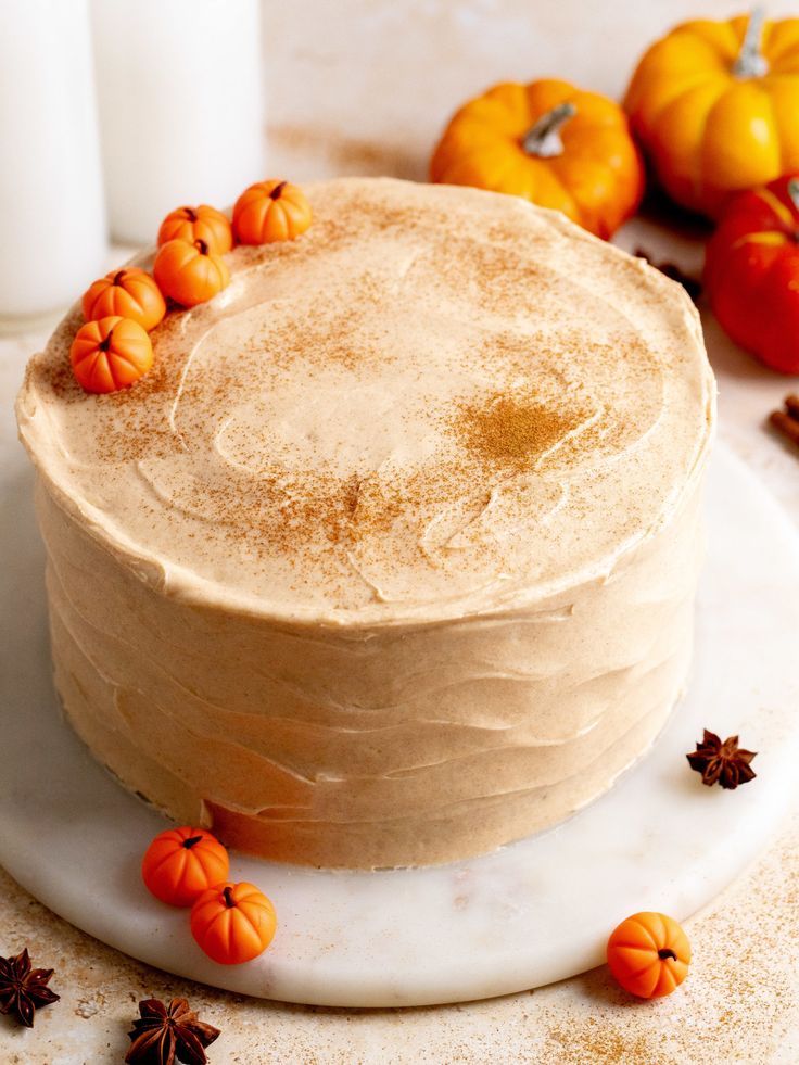 Pumpkin spice cake with cream frosting, topped with mini pumpkins, surrounded by autumn decorations and star anise.