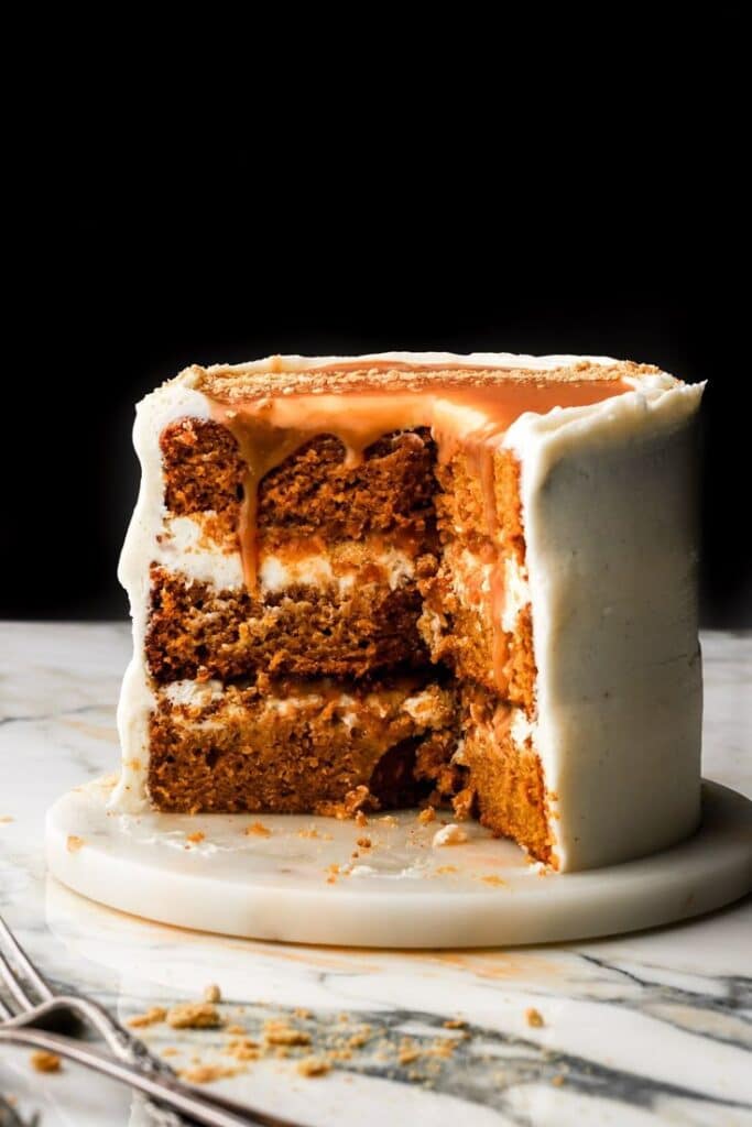 Four-layer spice cake with creamy frosting and a caramel glaze on a marble surface, partially sliced.