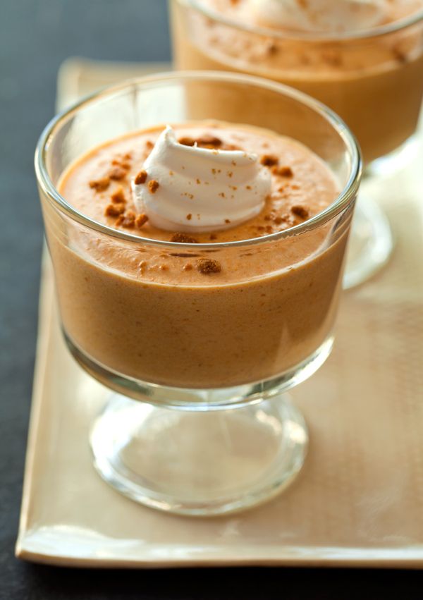 Creamy pumpkin mousse dessert in a glass topped with whipped cream and sprinkled cookies on a tray.