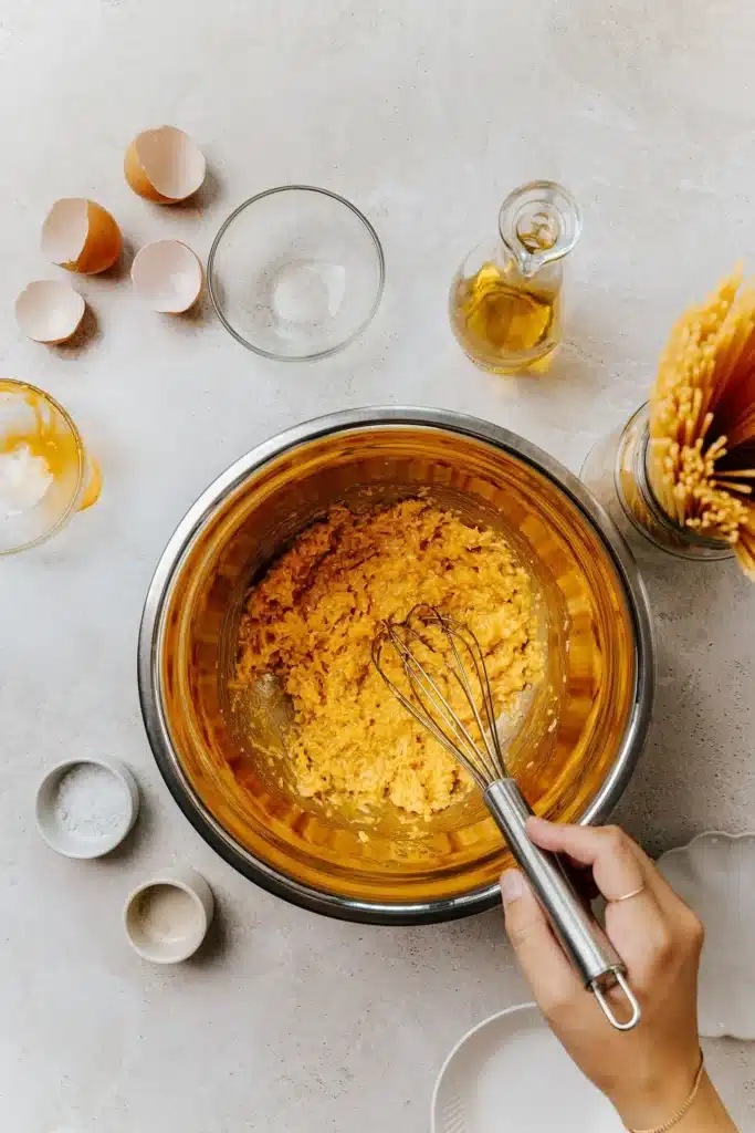 Mixing pasta dough ingredients: eggshells, flour, oil, spaghetti on countertop. Perfect for homemade pasta recipes.