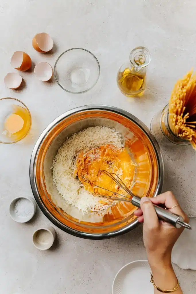 Mixing ingredients for homemade pasta in a bowl with cheese, eggs, and olive oil on a kitchen counter.