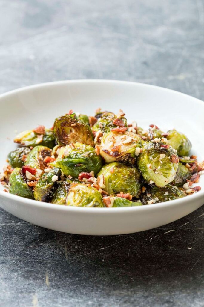 Roasted Brussels sprouts with crispy bacon in a white bowl on a dark stone table.