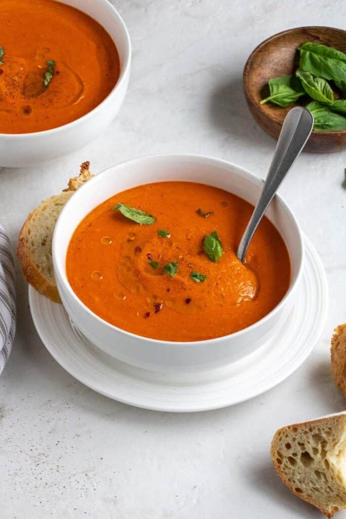 Bowl of creamy tomato soup garnished with basil, served with fresh bread. Perfect for a cozy meal.