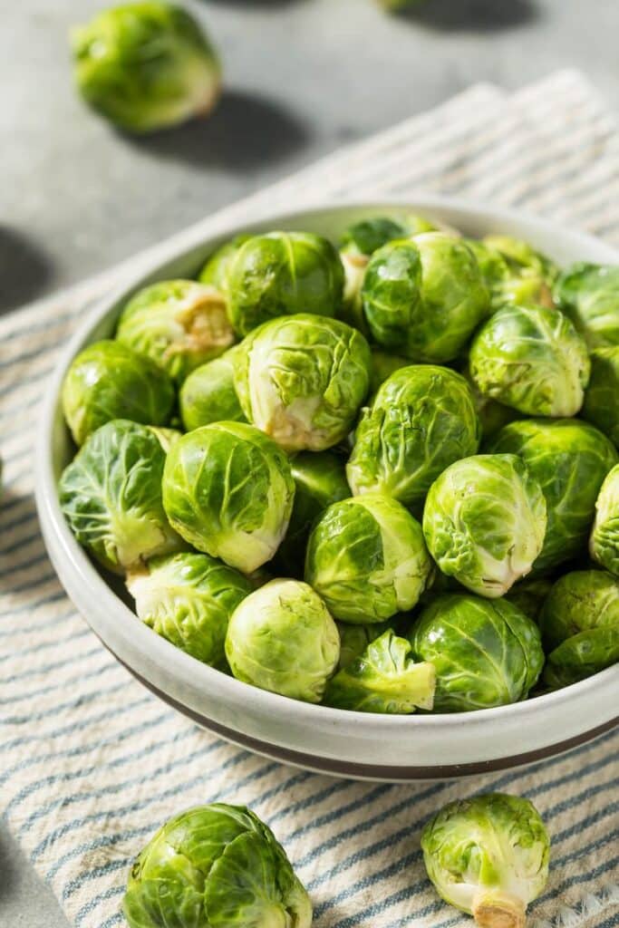 Bowl of fresh Brussels sprouts on a striped cloth, ready for cooking and healthy meal preparation.