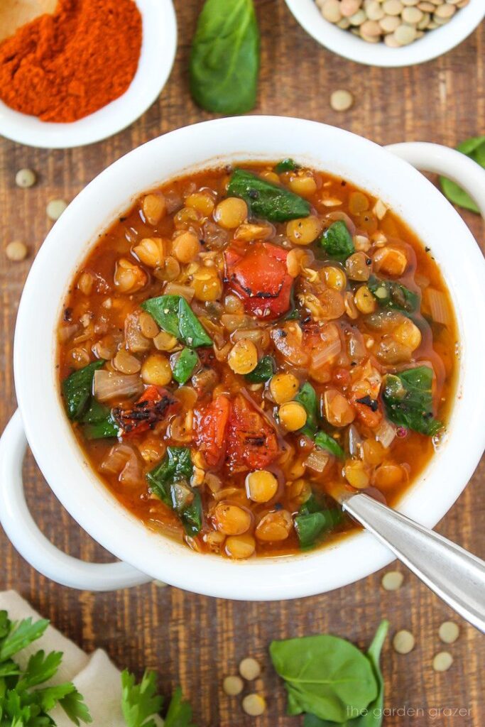 Hearty lentil and vegetable soup in a white bowl with fresh ingredients on wooden table.