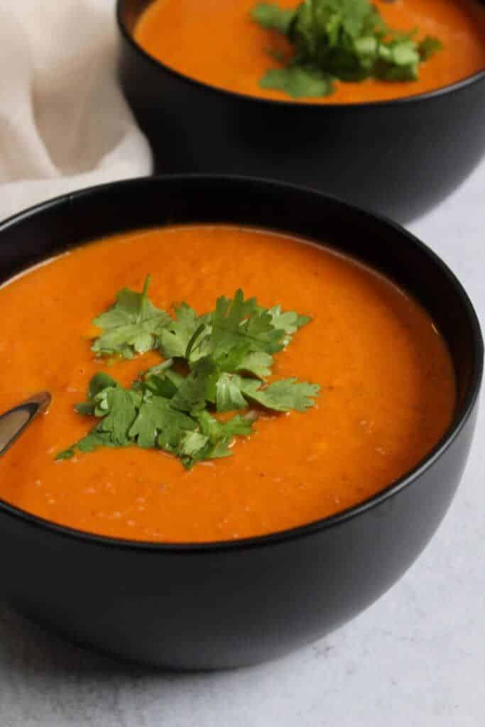 Creamy tomato soup garnished with fresh cilantro in black bowls, perfect for a cozy meal.