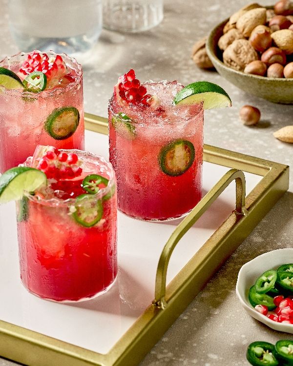 SpicyPomegranateGingerFizz - 10 Crowd-Pleasing Appetizers That Will Wow Your Party | Three vibrant pomegranate jalapeño cocktails garnished with lime on a tray, perfect for a refreshing drink setup.
