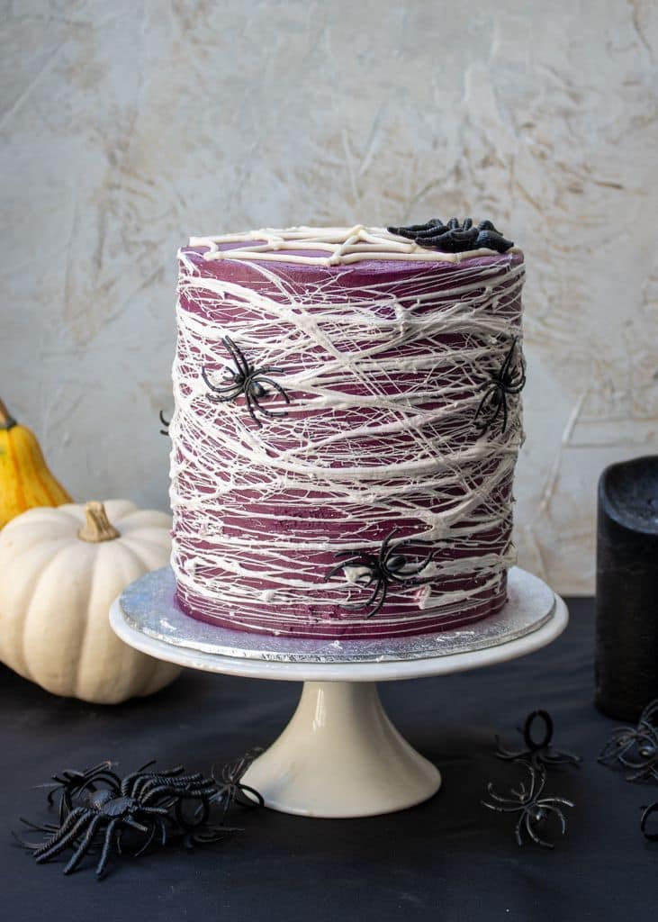 Halloween-themed cake with white web-like frosting and black spider decorations on a cake stand.