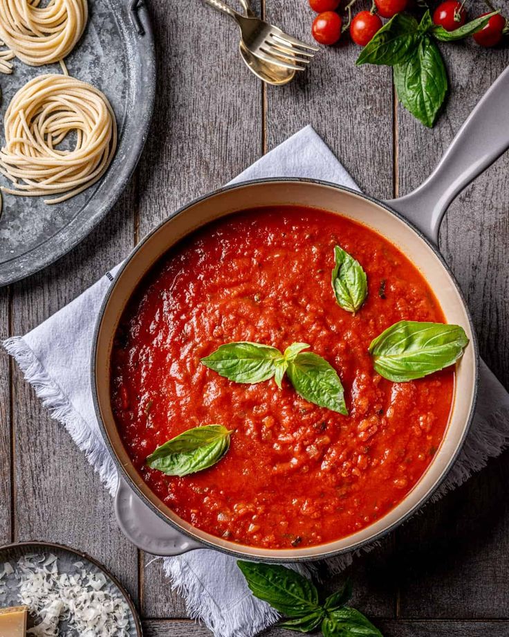 Fresh tomato sauce with basil in a pan, surrounded by pasta nests, cherry tomatoes, and grated cheese.