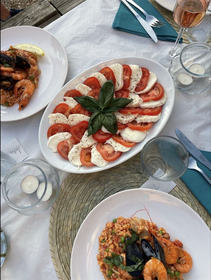 Screenshot - 10 Crowd-Pleasing Appetizers That Will Wow Your Party | Caprese salad with tomatoes, mozzarella, and basil beside seafood risotto, set on an elegant outdoor table.