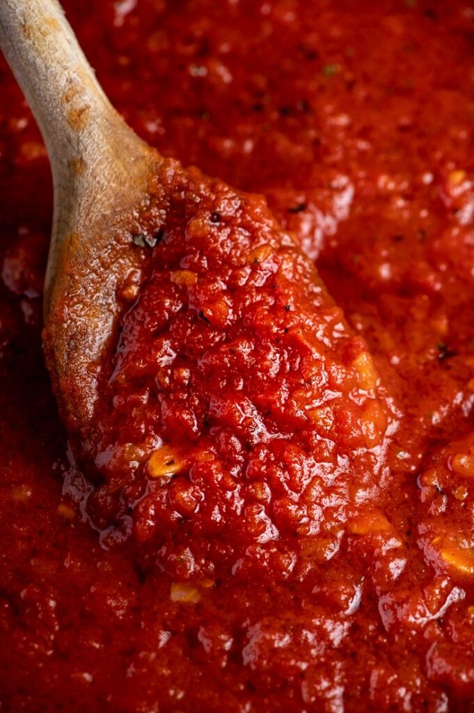 Rich homemade tomato sauce being stirred with a wooden spoon.