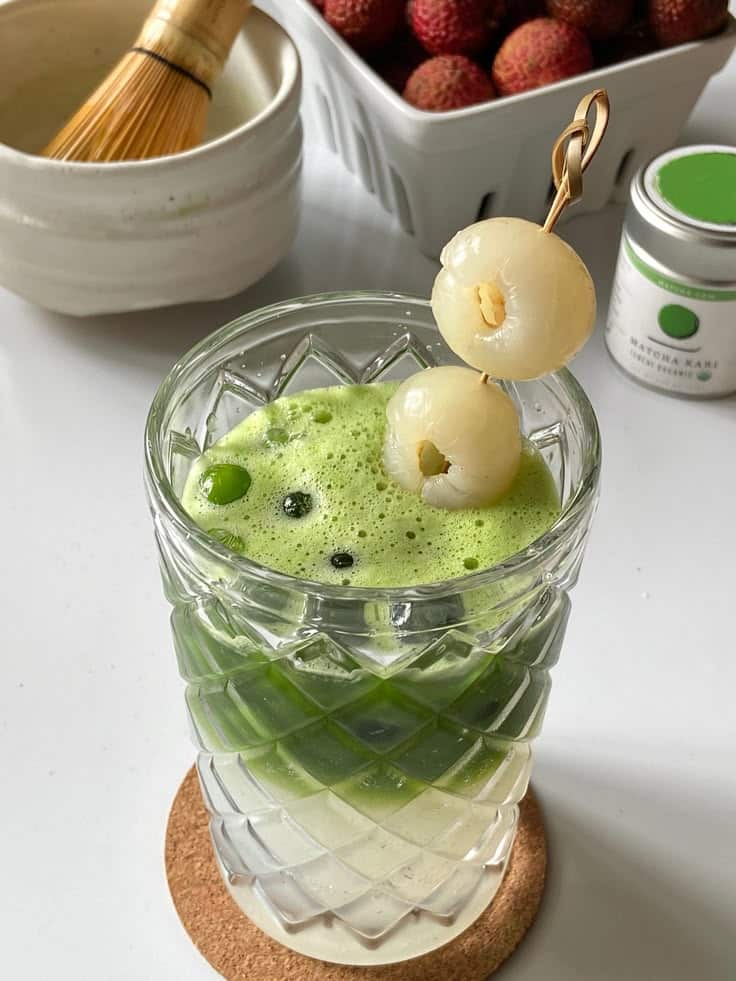 Sweet Refreshing Iced Lychee Matcha Recipe - 10 Crowd-Pleasing Appetizers That Will Wow Your Party | Refreshing matcha drink with lychee garnish on skewers, surrounded by whisk and fruits.
