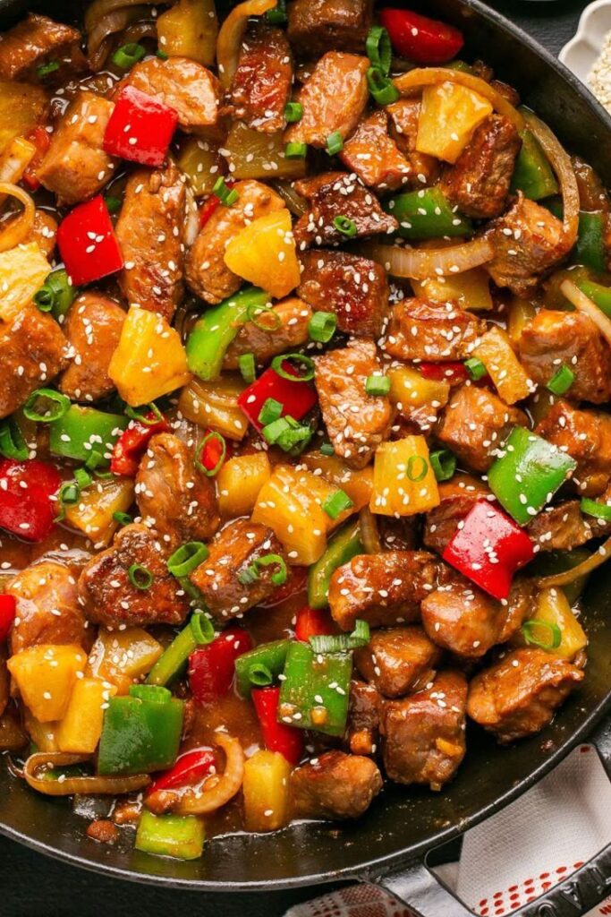 Delicious sweet and sour pork with colorful bell peppers, pineapple, and sesame seeds in a savory sauce.