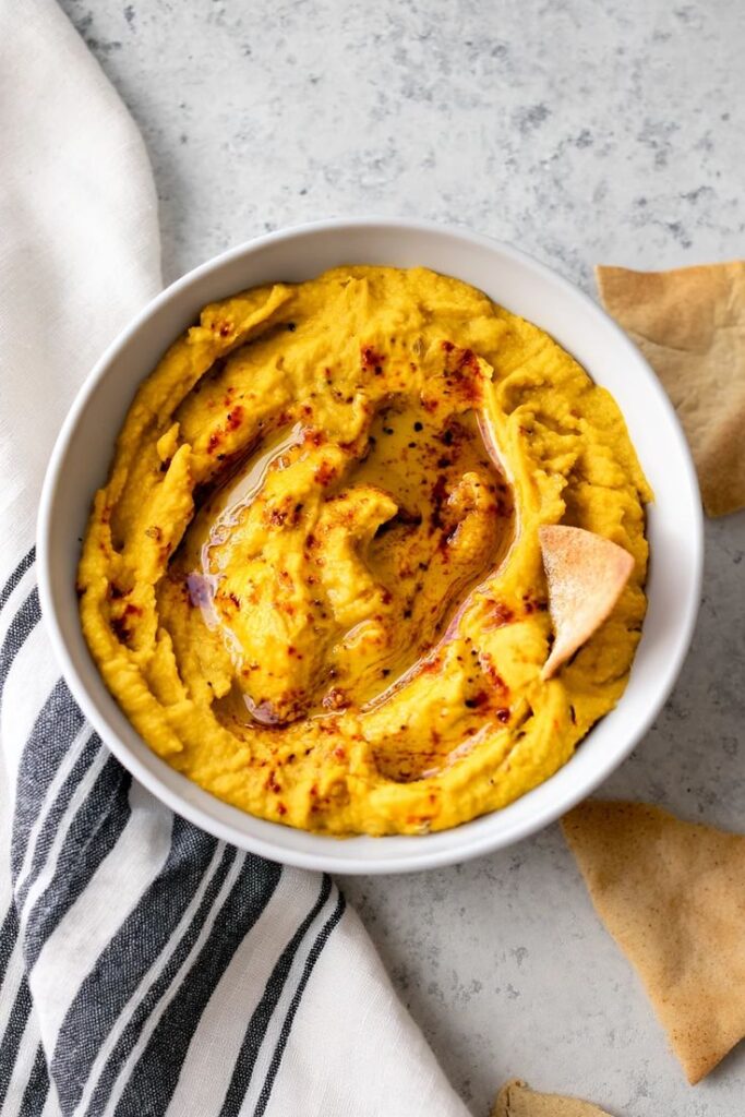 Creamy pumpkin hummus with a drizzle of oil and pita chips in a white bowl. Perfect fall appetizer!