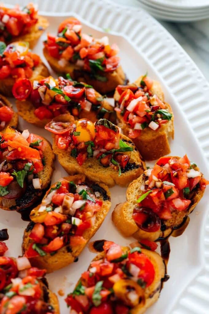 Tomato Basil Bruschetta with Balsamic Drizzle - 10 Crowd-Pleasing Appetizers That Will Wow Your Party | Plate of vibrant tomato bruschetta on toasted baguette slices with basil and balsamic drizzle.