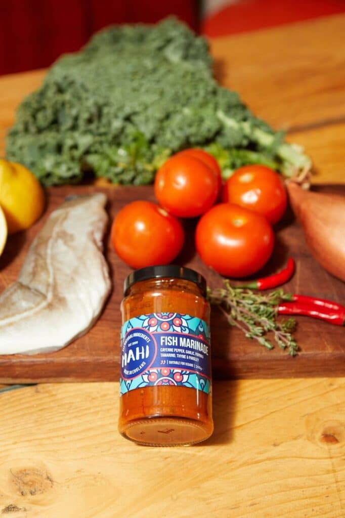 Fish marinade jar with fresh tomatoes, kale, fish fillet, chili, and herbs on a wooden table.