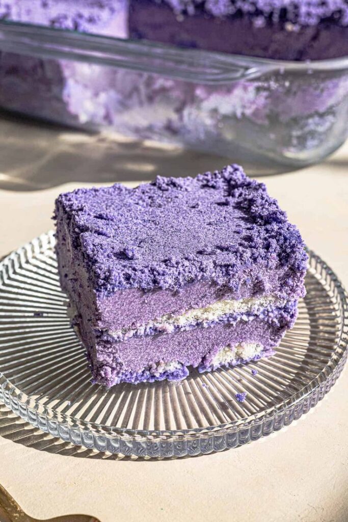 Purple yam cake slice on a glass plate, showcasing layered ube flavor. Vibrant, moist, and perfect for dessert lovers.