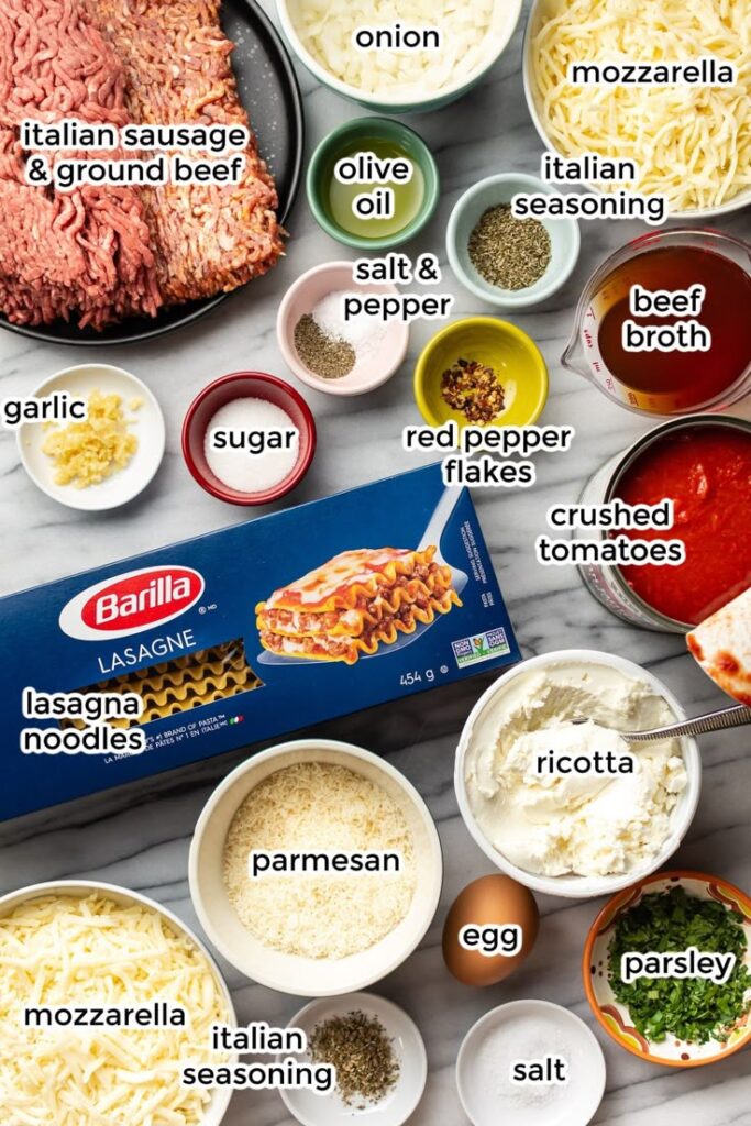 Lasagna ingredients: meat, noodles, cheese, spices, tomatoes, egg, and herbs on a kitchen countertop.