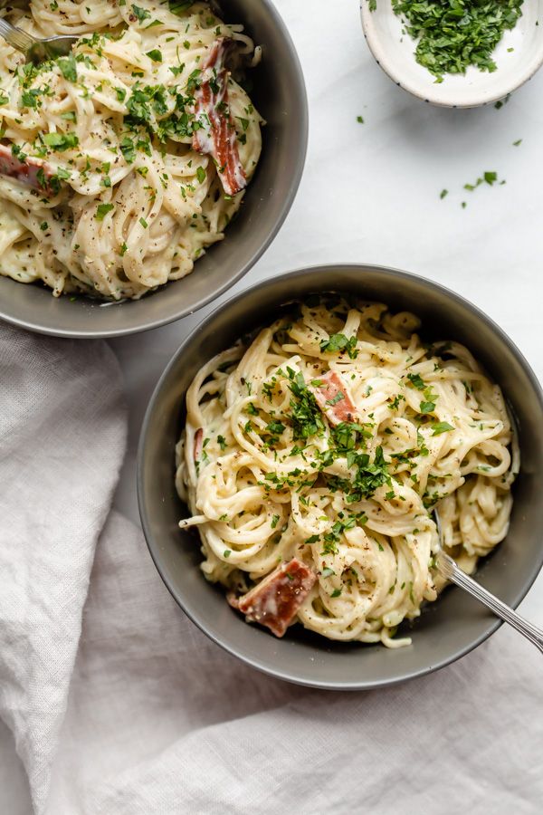 Two bowls of creamy pasta topped with parsley and bacon.