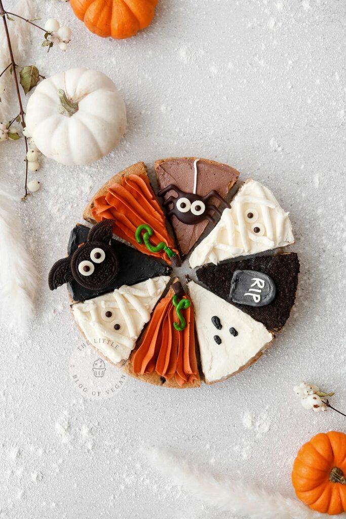 Halloween-themed cheesecake topped with spider, ghost, and pumpkin decorations, surrounded by small pumpkins.
