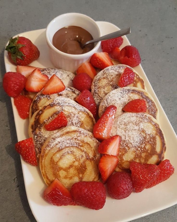 Fluffy pancakes with strawberries and raspberries, served with chocolate sauce on a white plate.