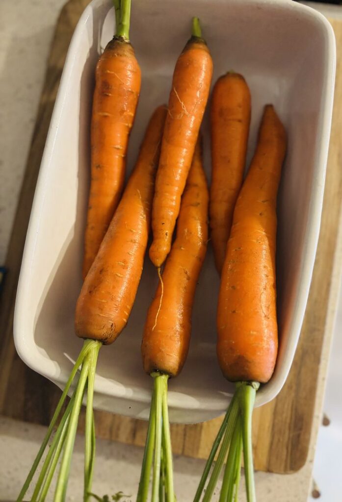 Fresh organic carrots in a white dish on a wooden cutting board.