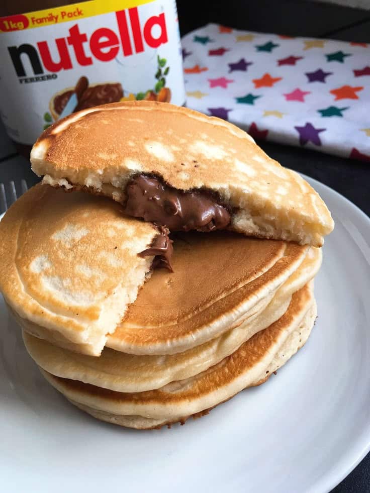 Fluffy pancakes filled with creamy Nutella on a white plate, perfect for breakfast or brunch delight.