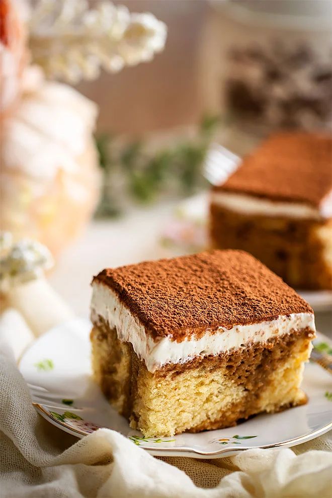 Slice of delicious tiramisu cake with creamy layers and cocoa topping on a decorative plate, perfect dessert treat.