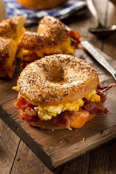Bagel sandwich with crispy bacon, scrambled eggs, and cheese on a wooden board, perfect breakfast delight.