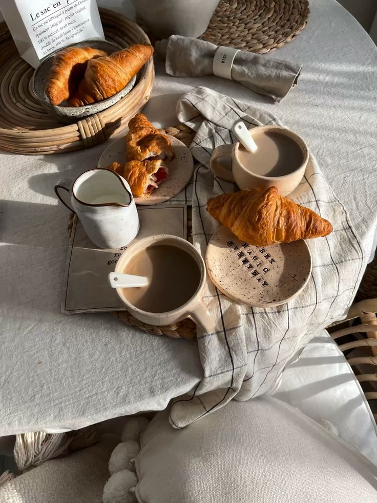 Cozy breakfast scene with fresh croissants, coffee, and cream on a sunlit table with a woven basket and linen napkin.