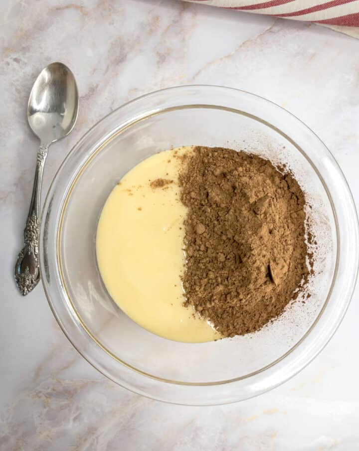Bowl with cocoa powder and custard on a marble surface, silver spoon beside. Ideal for dessert recipes.