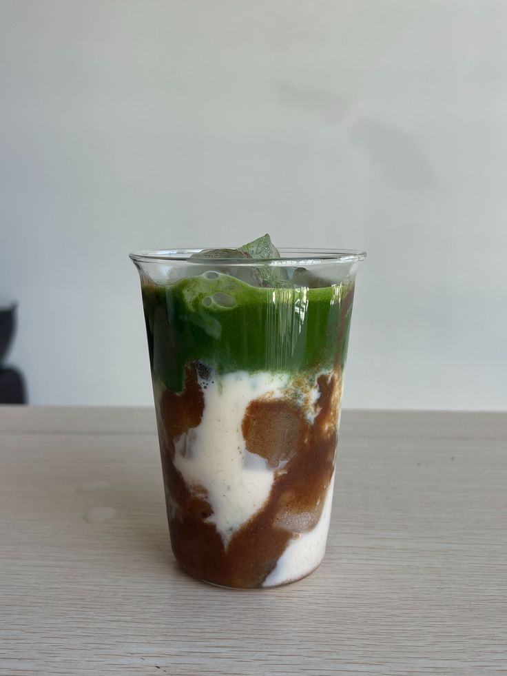 Iced matcha latte with layers of green tea, milk, and espresso in a clear glass on a wooden table.