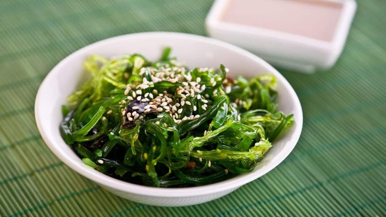 p0h2rjhc - Unlock Better Ice Cream: The Surprising Benefits of Seaweed| Bowl of fresh seaweed salad topped with sesame seeds on a green mat background.