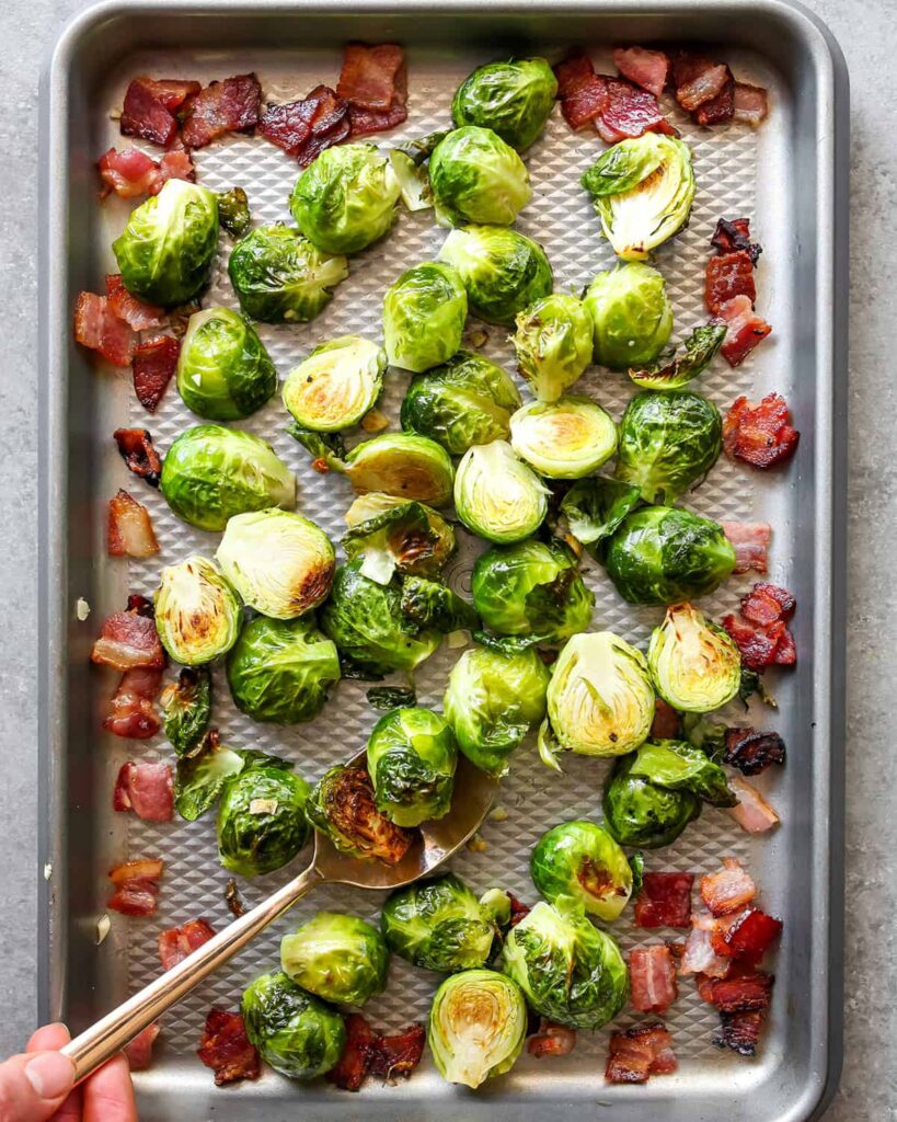 Roasted Brussels sprouts with crispy bacon on a baking sheet, perfect for a delicious side dish.